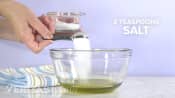 2 teaspoons of salt being poured into a bowl.